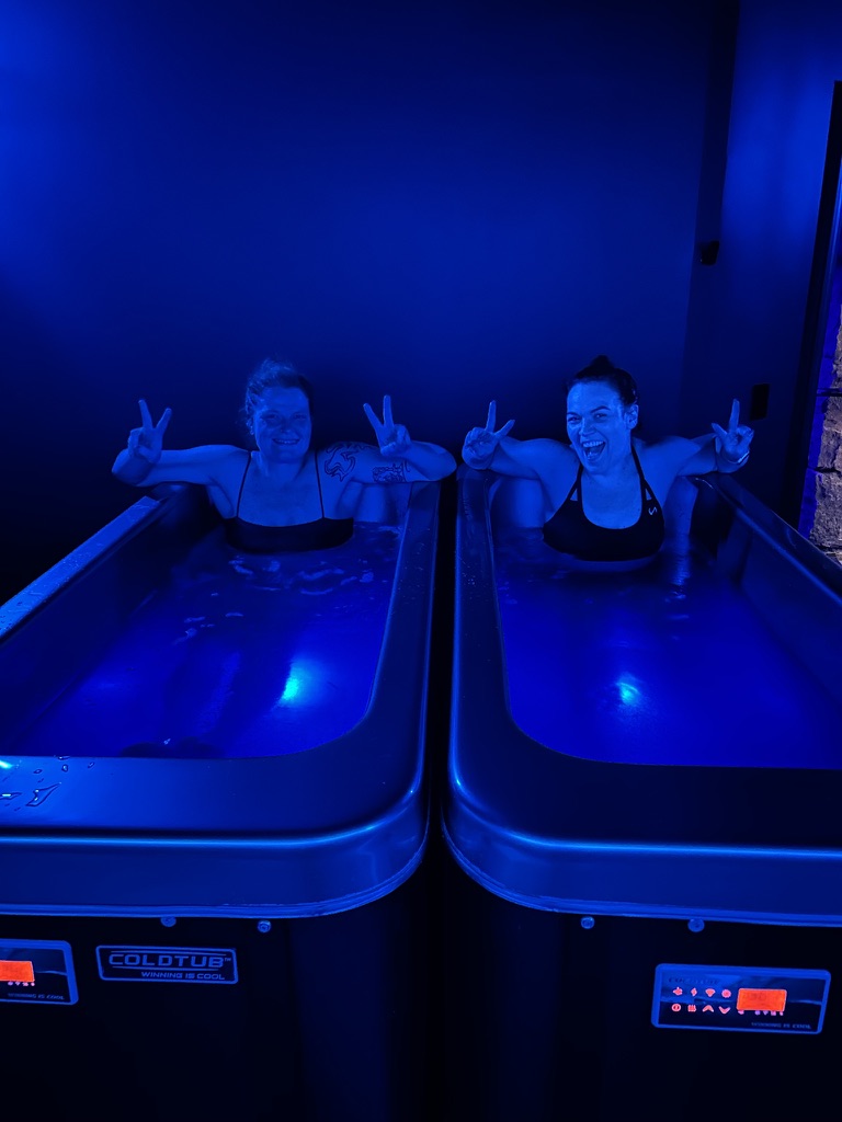Two women smiling in the cold plunge tubs at MindFuel