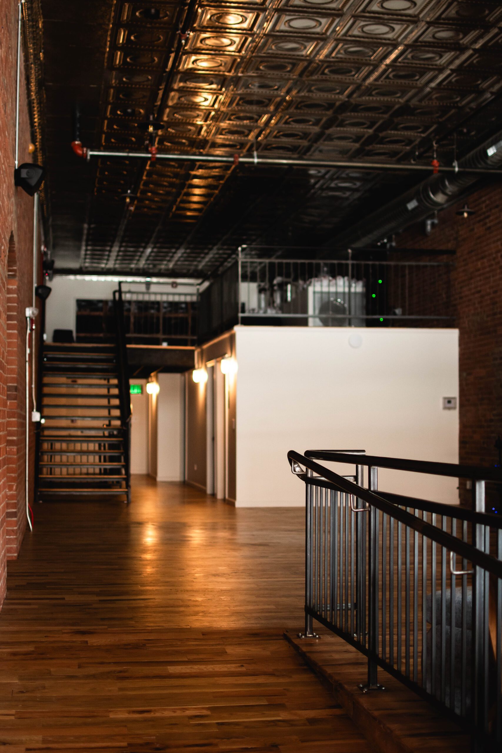 Recovery Lounge mezzanine at MindFuel Method featuring warm lighting, tin ceiling, exposed brick, and hardwood floors in Pittsburgh's Strip District